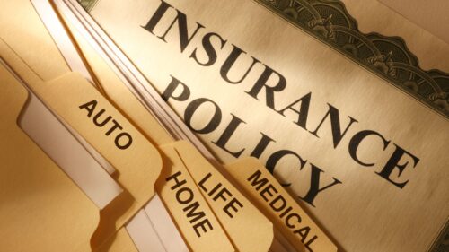 A picture of an insurance policy in the background with four manilla folders labeled auto, home, life, and medical on top of the insurance policy.
